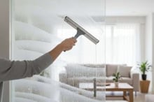 Hand using squeegee to clean interior glass doors | How to Clean Interior Glass Doors and Keep Them Spotless