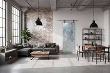Industrial loft interior with exposed brick wall, large windows, and a frosted glass barn door featuring abstract carved design — modern, handcrafted glass barn doors by Sans Soucie Art Glass for open loft living.