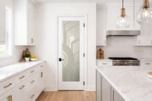 Modern glass pantry door with geometric Sun Odyssey design in a bright contemporary kitchen with gold hardware and marble island.