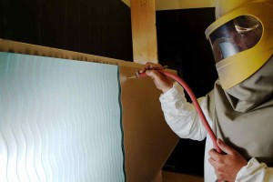 Sans Soucie Glass artist sandblasting waves into a glass panel that will become a window.