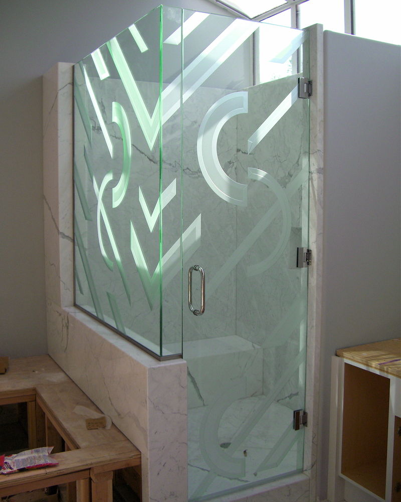 A stunning etched and carved glass shower enclosure with geometric shapes of half circles and bands.  The outside perimeter edges have been sculpture carved, with the insides lightly frosted or misted for a nice contrast.