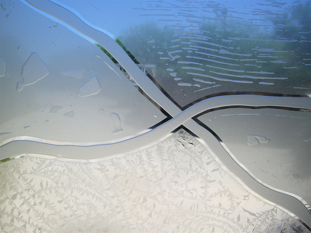 Close-up of a decorative glass partition panel showcasing flowing abstract landscape patterns with carved glass contours, frosted sections, and textured glue chip glass details.