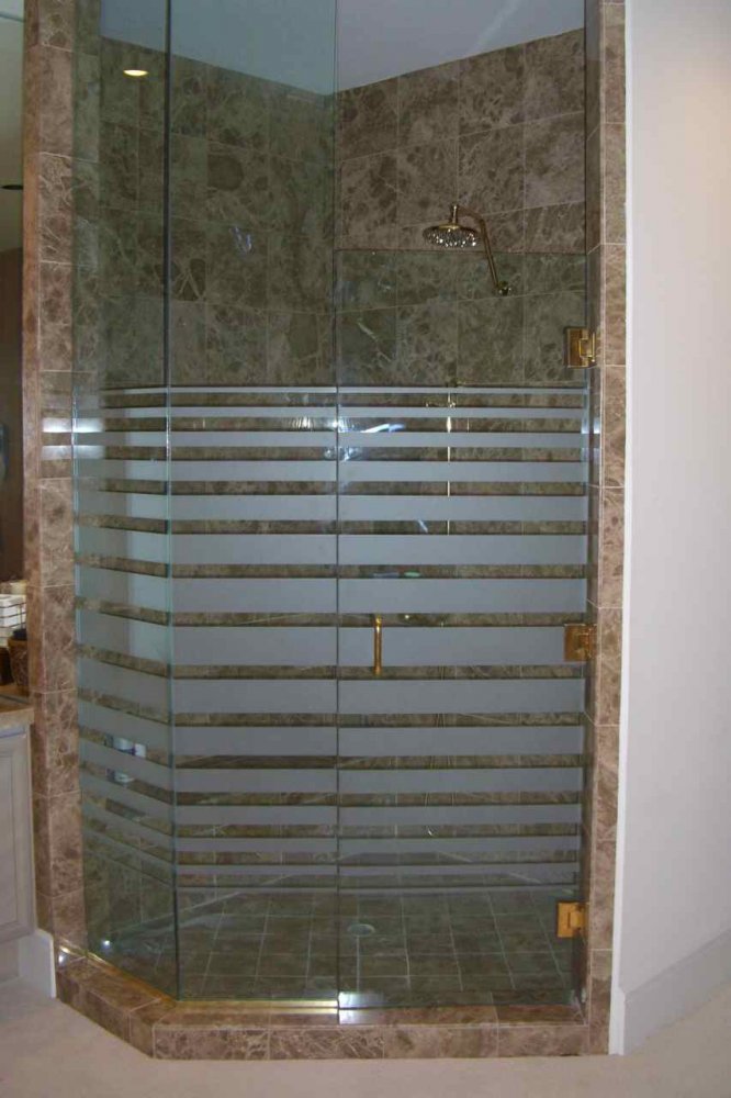 Clear glass shower door and enclosure with horizontal frosted stripe design, brass hardware, and stone tile shower walls.
