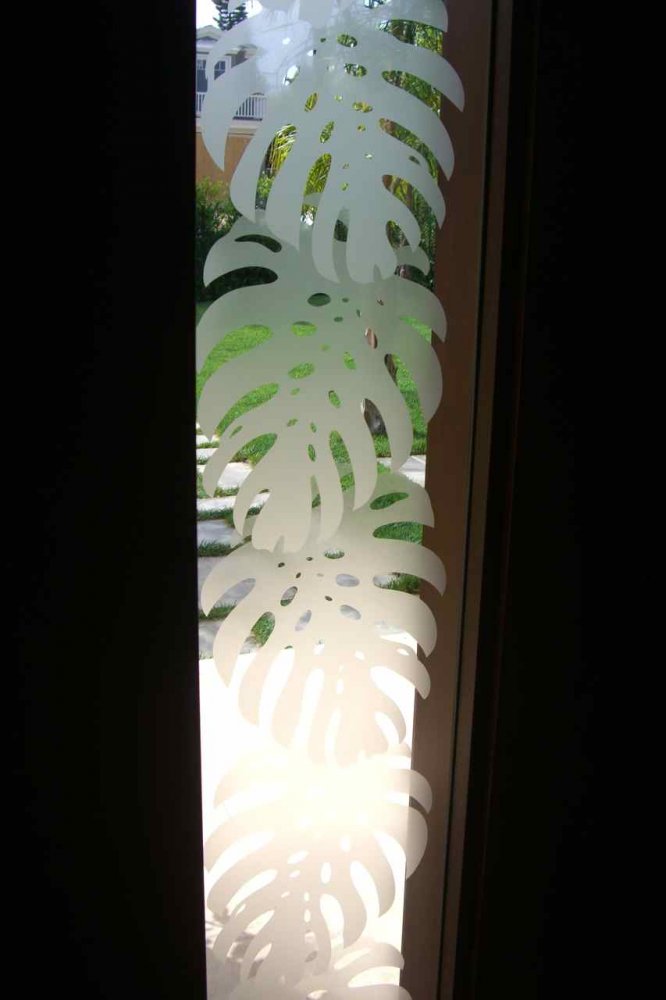 Close-up of etched monstera leaf design on frosted glass sidelight panel with natural light shining through.