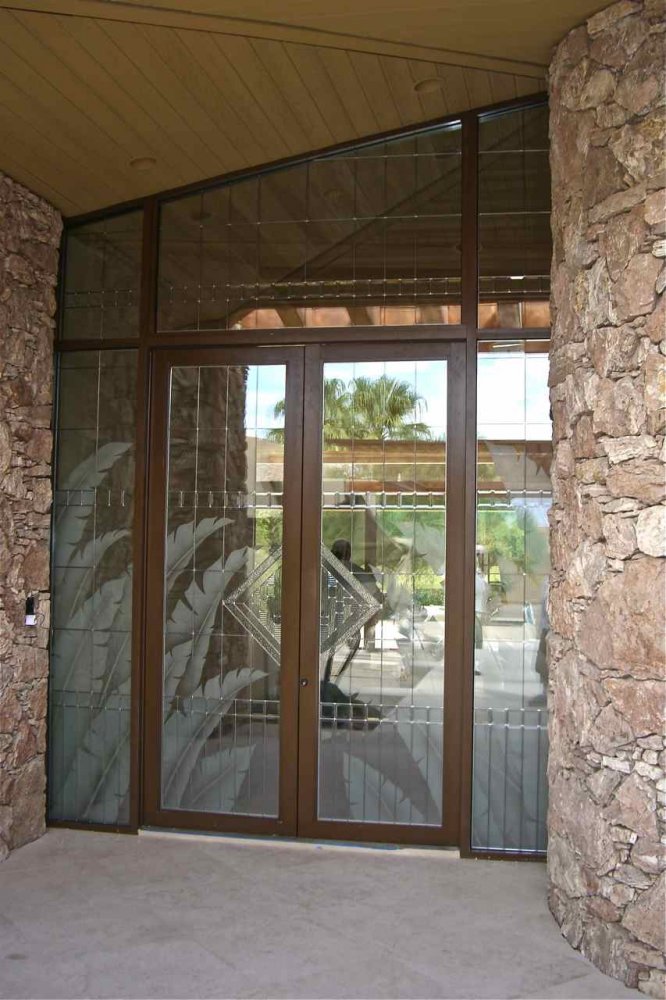 etched glass double front doors with sidelights and transom featuring geometric and palm leaf design in a modern stone entryway