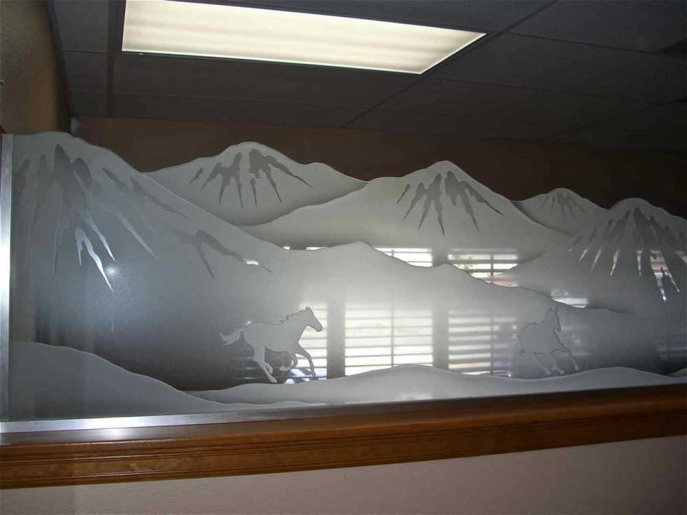 Custom etched glass pony wall divider with carved horses running through landscape scene used as interior partition