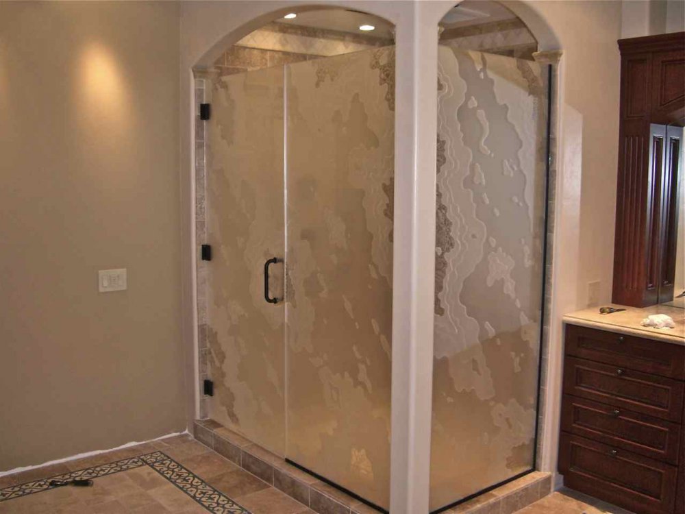 Large decorative frosted glass shower enclosure with an abstract carved pattern, black hardware, and warm traditional bathroom finishes.