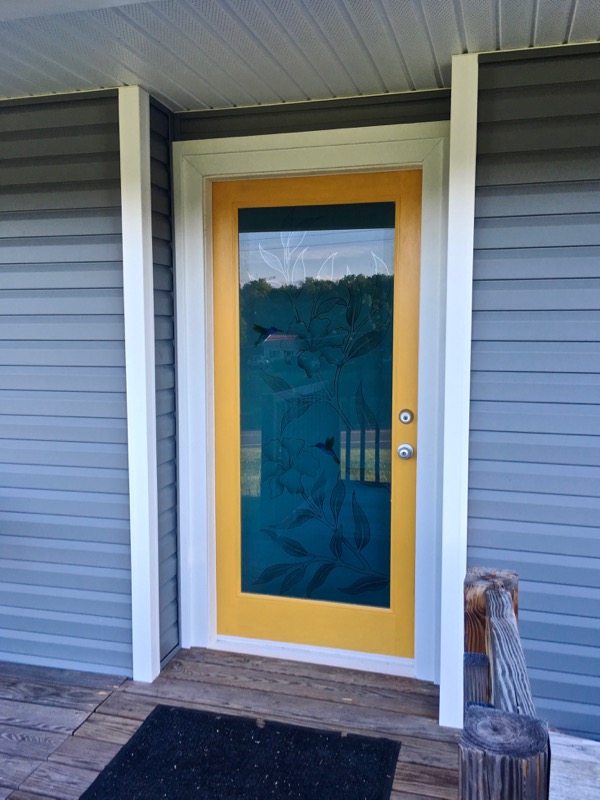 Full view of the new yellow glass front door with custom hibiscus and hummingbird artwork on the glass panel.