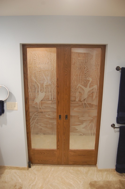 Wood pocket pantry doors with frosted glass panels featuring cranes, cattails, and a wetland scene
