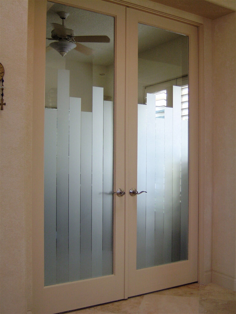 White double interior doors with frosted glass panels featuring a vertical geometric pattern, separating rooms while providing privacy