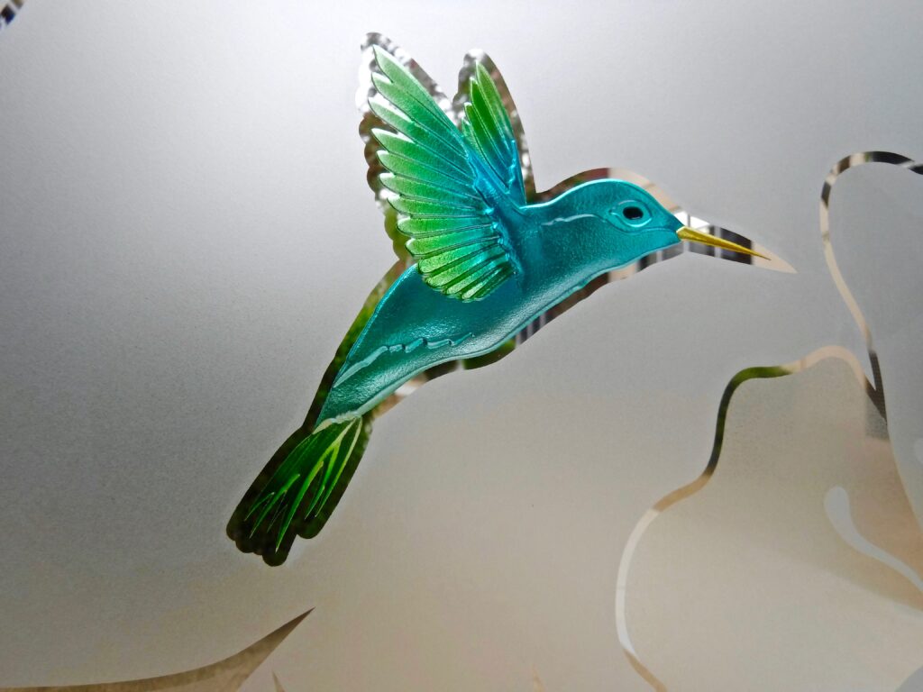 Etched glass hummingbird with clear and frosted details showing color variation from lighting and background reflection
