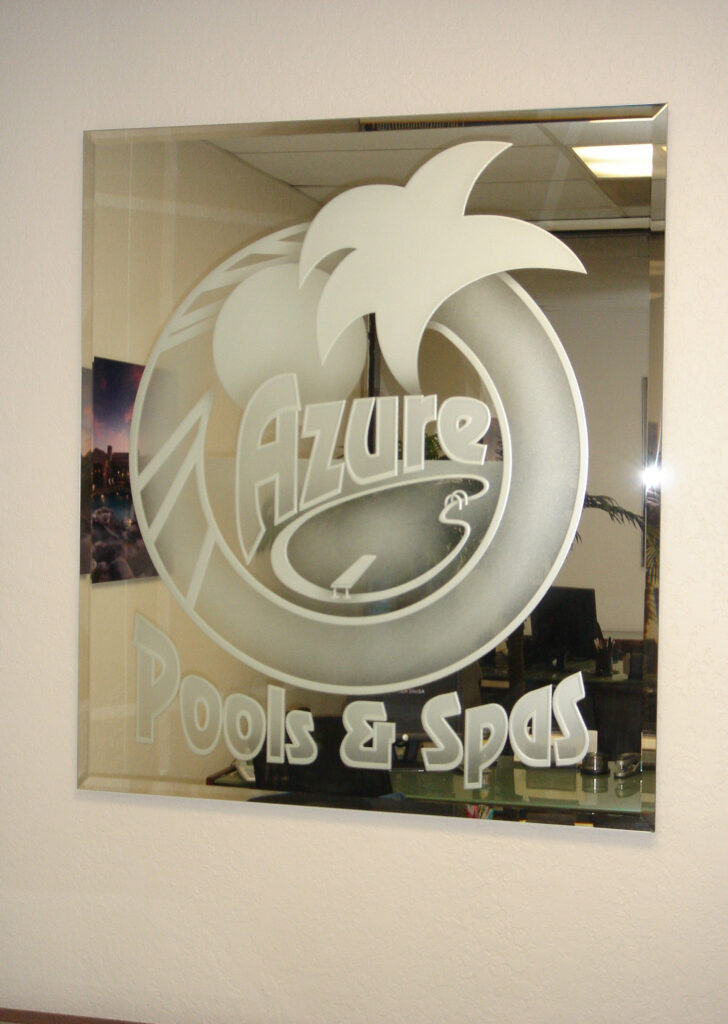 Etched glass logo sign for Azure Pools and Spas mounted on light wall surface, demonstrating contrast between frosted design and neutral background