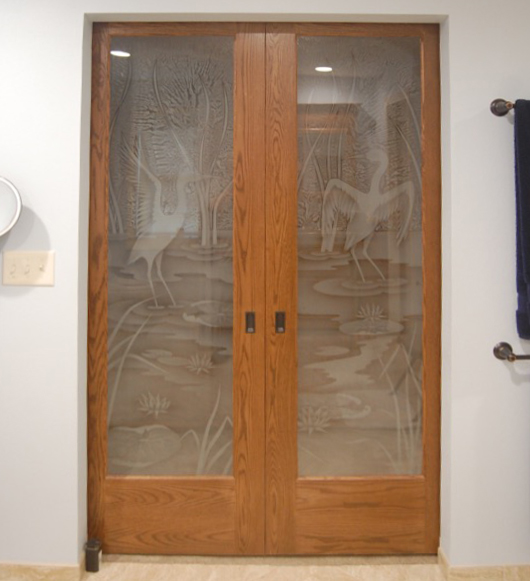 Wood-framed frosted glass bathroom doors with etched crane and pond artwork for a luxury spa-style interior
