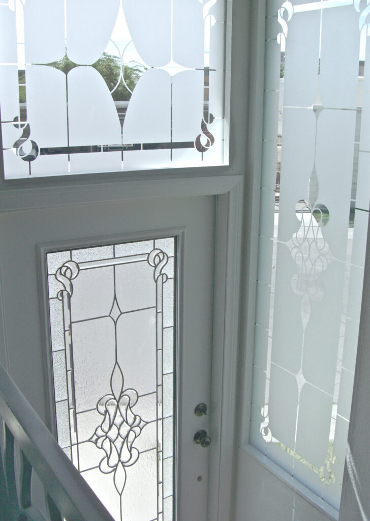 Interior view of a white front door with frosted glass panel and matching frosted glass sidelights, featuring an elegant etched pattern for privacy.