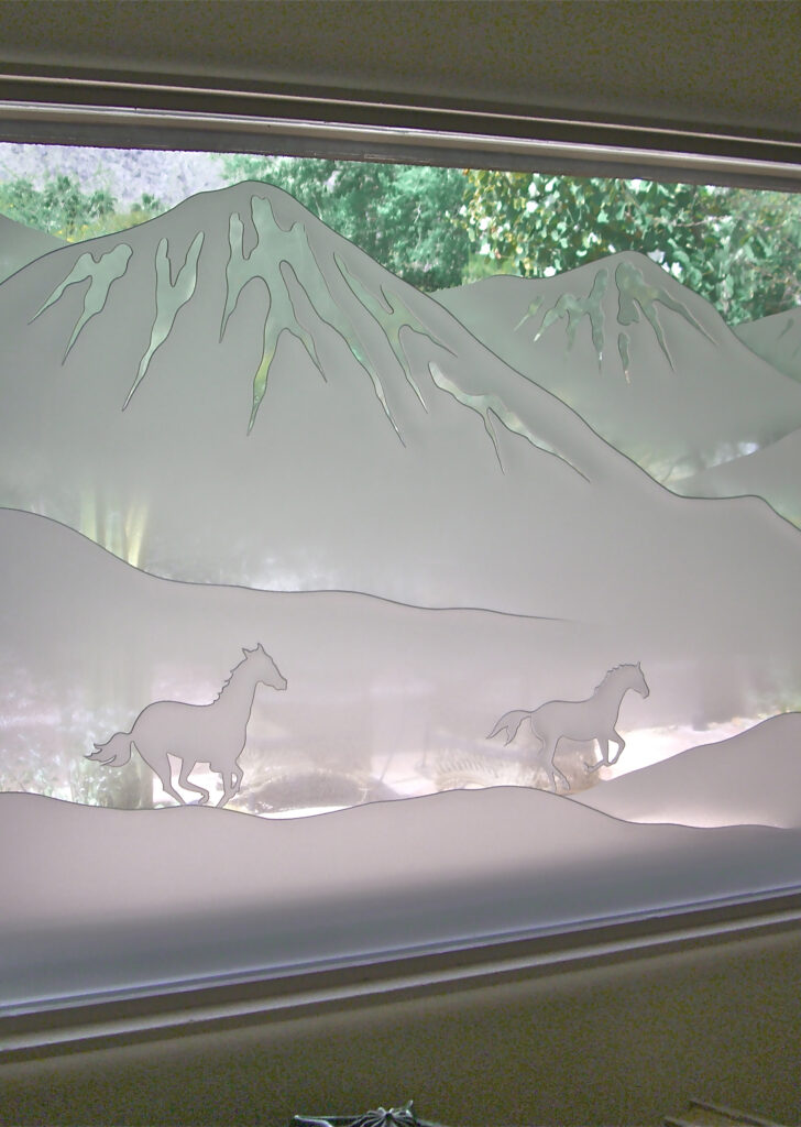 Etched glass window with mountain landscape and galloping horses offers privacy while still allowing natural light into the space