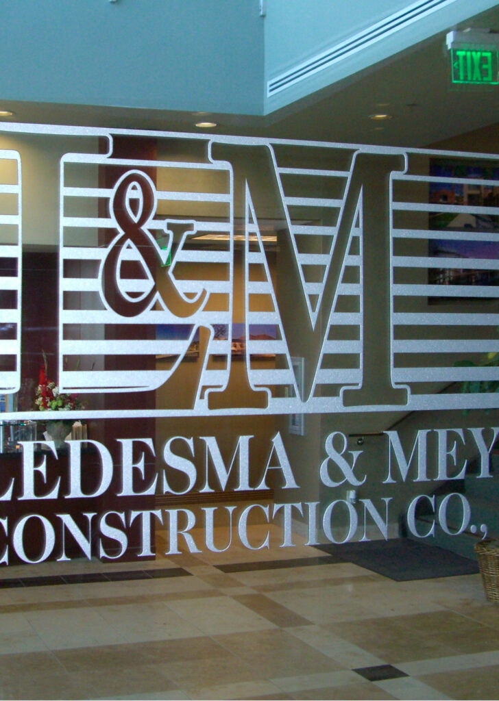 Decorative glass wall panel with etched company logo and lettering, custom glass signage for office identification