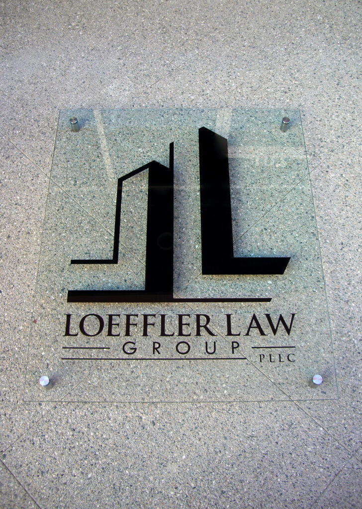 Custom etched glass wall with Loeffler Law Group logo mounted on standoffs, showcasing branded corporate glass design with a sleek modern appearance.