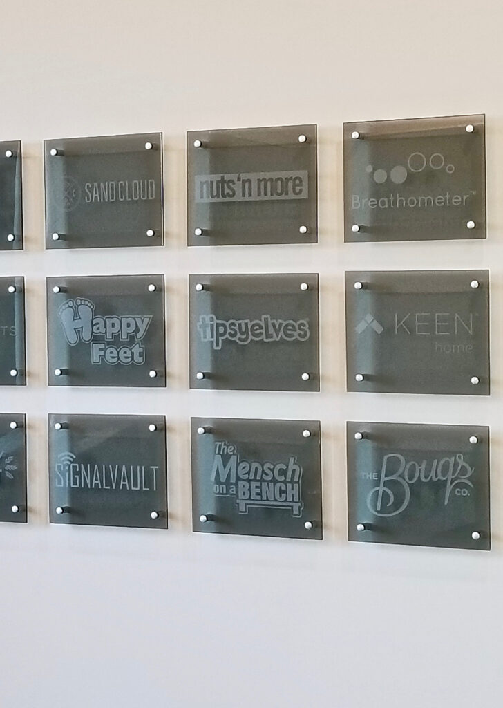 Frosted glass wall panels featuring multiple company logos, creating a branded corporate identity display with sophisticated modern office aesthetics.
