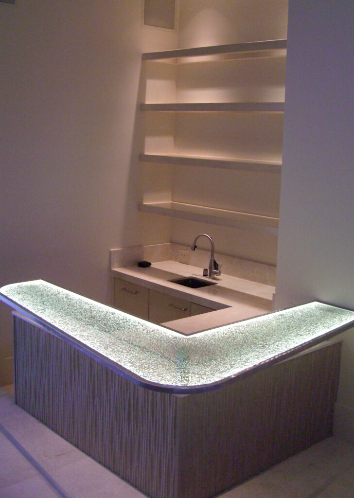 edge-lit glass bar counter with textured shattered glass surface glowing with integrated LED lighting