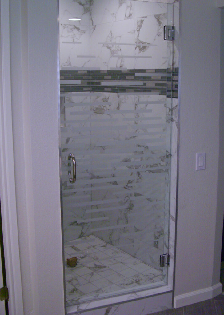 Frameless shower door with horizontal frosted glass stripe pattern creating privacy in a modern marble tile bathroom