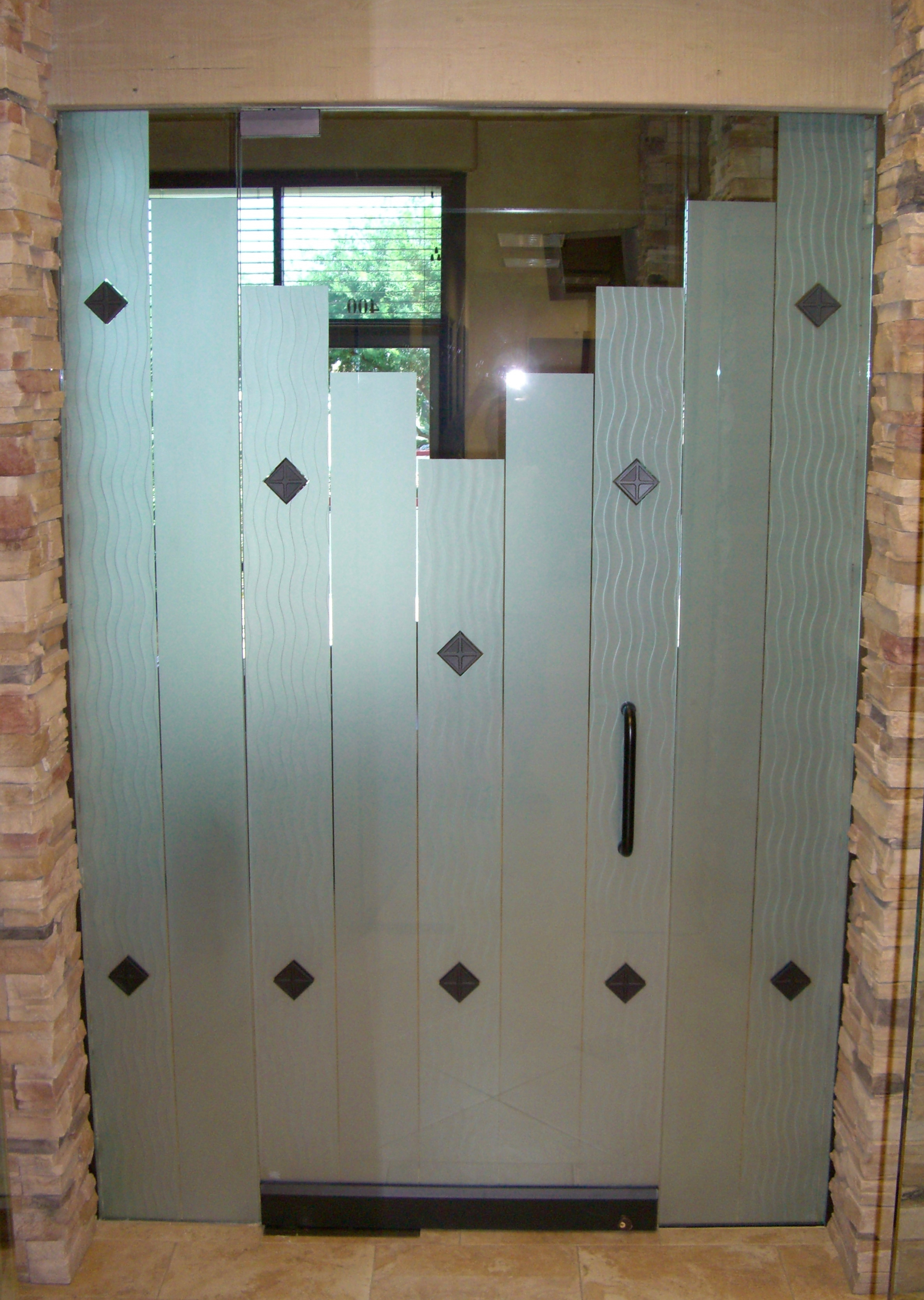 Frosted glass office door with stepped vertical panels and subtle wave texture, set between stone walls in a modern interior hallway