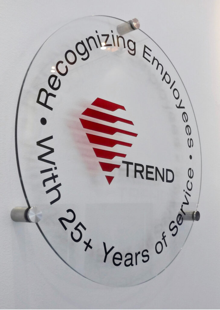 Round glass panel custom sign with etched lettering and red logo, mounted with stand-off hardware on wall surface for a sleek office display