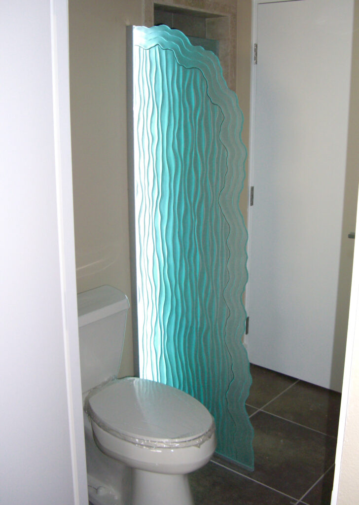 edge-lit carved glass shower divider with layered wave texture glowing with blue LED light in modern bathroom