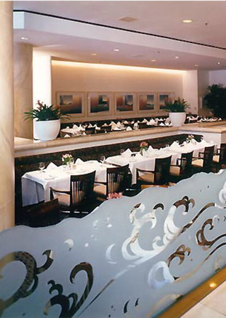 Decorative glass room partition with carved wave design separating restaurant dining areas