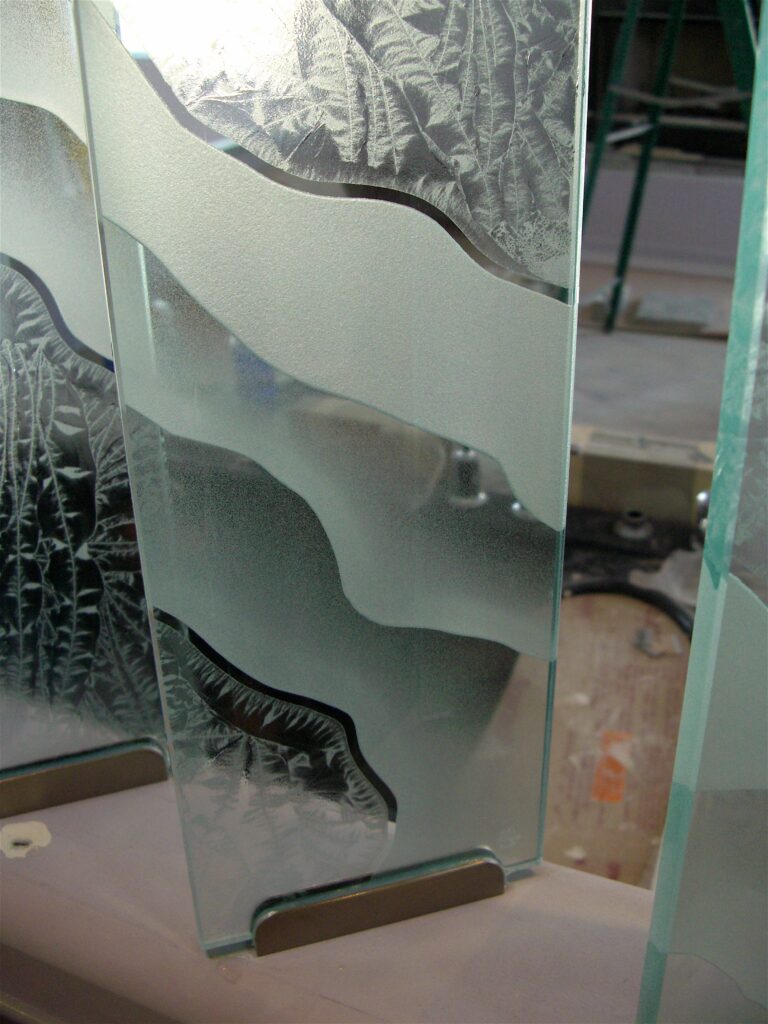 Close-up of a decorative glass partition panel showcasing custom shoreline patterns with alternating frosted bands and textured architectural glass details.