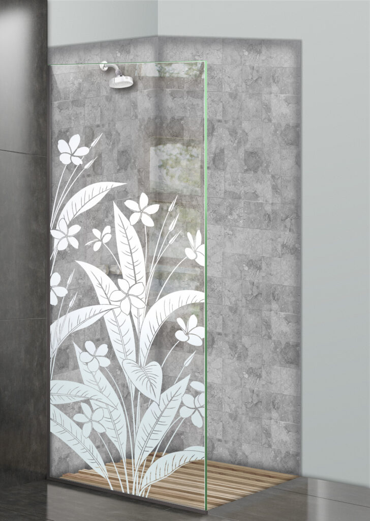 Glass shower divider with frosted plumeria flower and tropical leaf design in a gray tile shower.