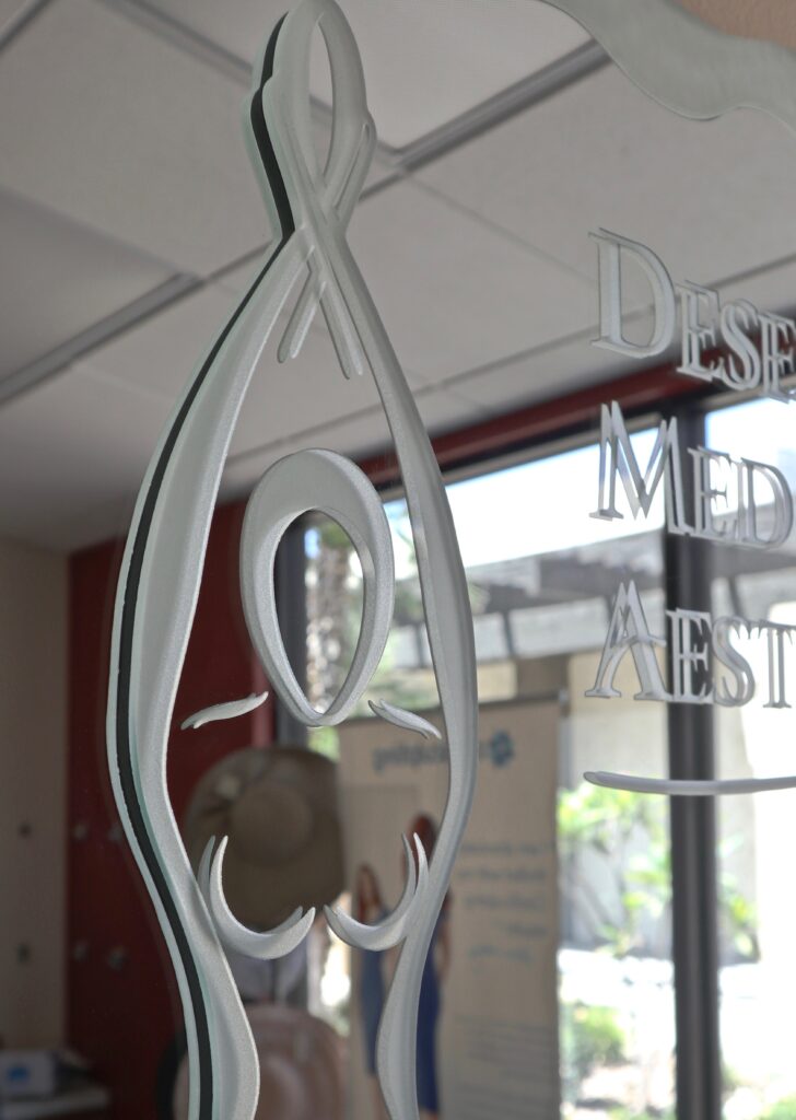 Etched glass office sign with frosted medical symbol and lettering on clear glass panel, installed on interior door for a clean professional look