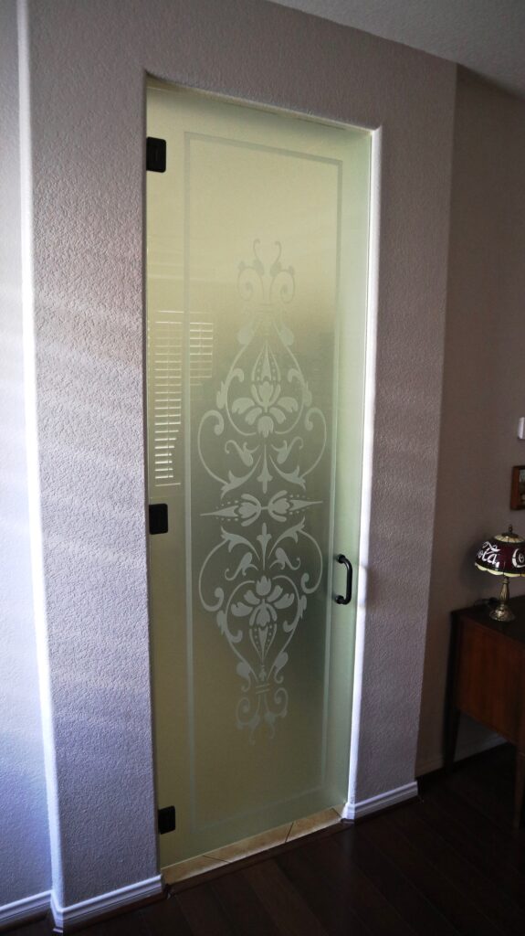 Frameless interior glass pantry door with elegant frosted scrollwork design, adding privacy and style to a compact kitchen entry