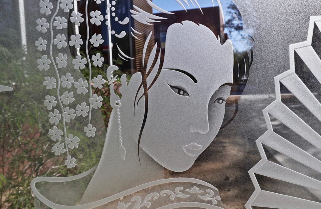 Close-up of 3D carved and etched glass panel showing geisha face with detailed shading and floral elements, highlighting precision sandblasted design