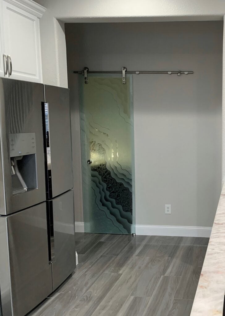 Sliding frosted glass barn door installed in compact kitchen pantry with contemporary etched abstract design