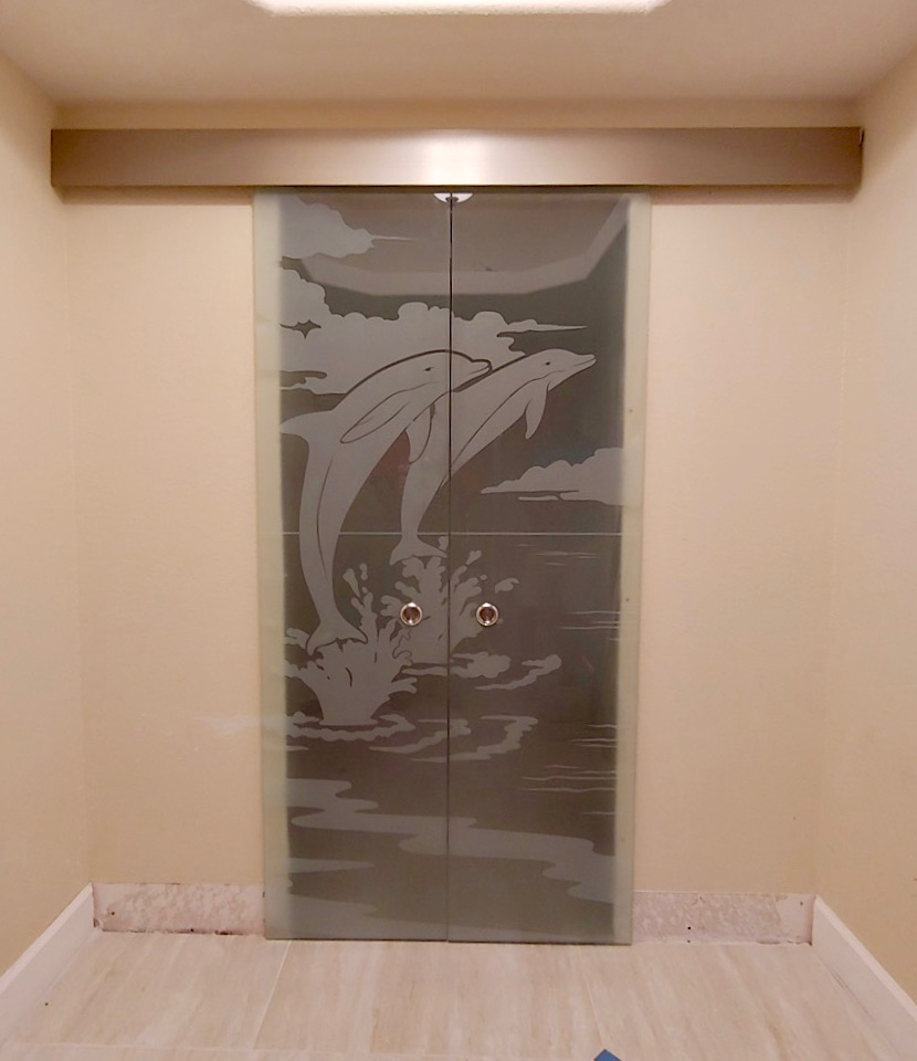 Pair of frosted interior sliding glass doors with a dolphin ocean design, creating a decorative room divider with a concealed sliding track.
