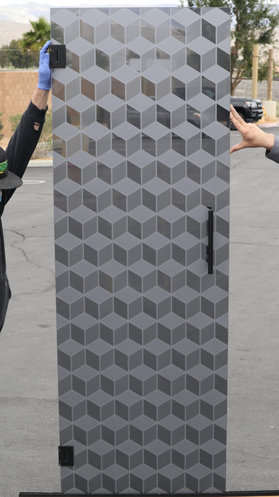 Decorative glass shower door featuring modern geometric cube pattern in frosted and gray etched glass.