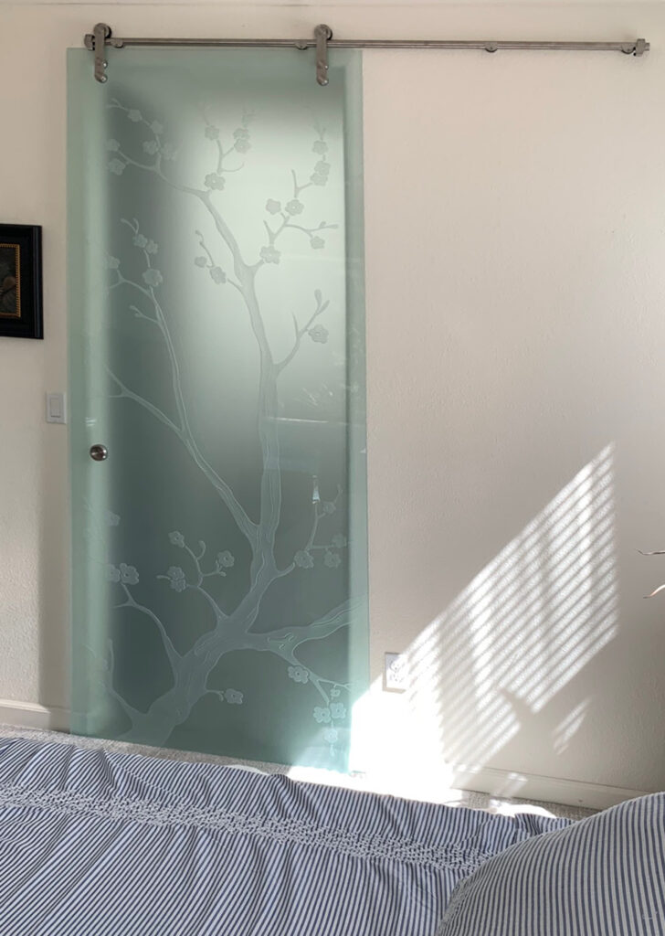 Frosted glass barn door with etched cherry blossom tree design in bedroom, decorative sliding glass interior door