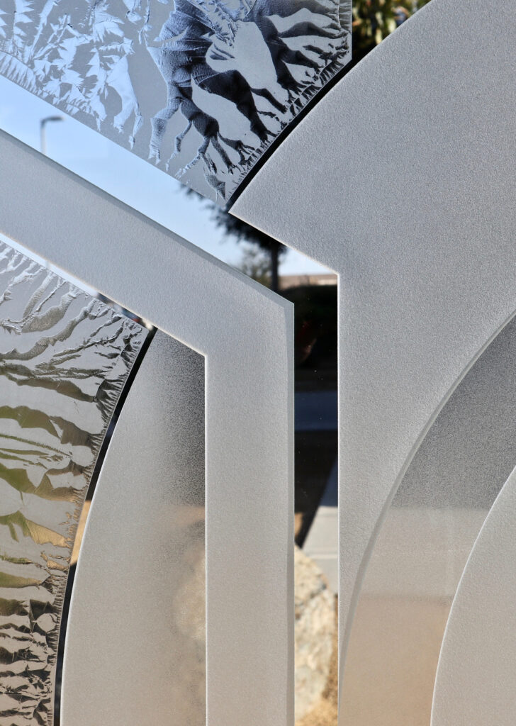 Close-up of Sun Odyssey, a sculpted frosted glass with layered curved geometry and textured accents, a refined design for a black front door with glass panels that delivers modern depth and privacy.