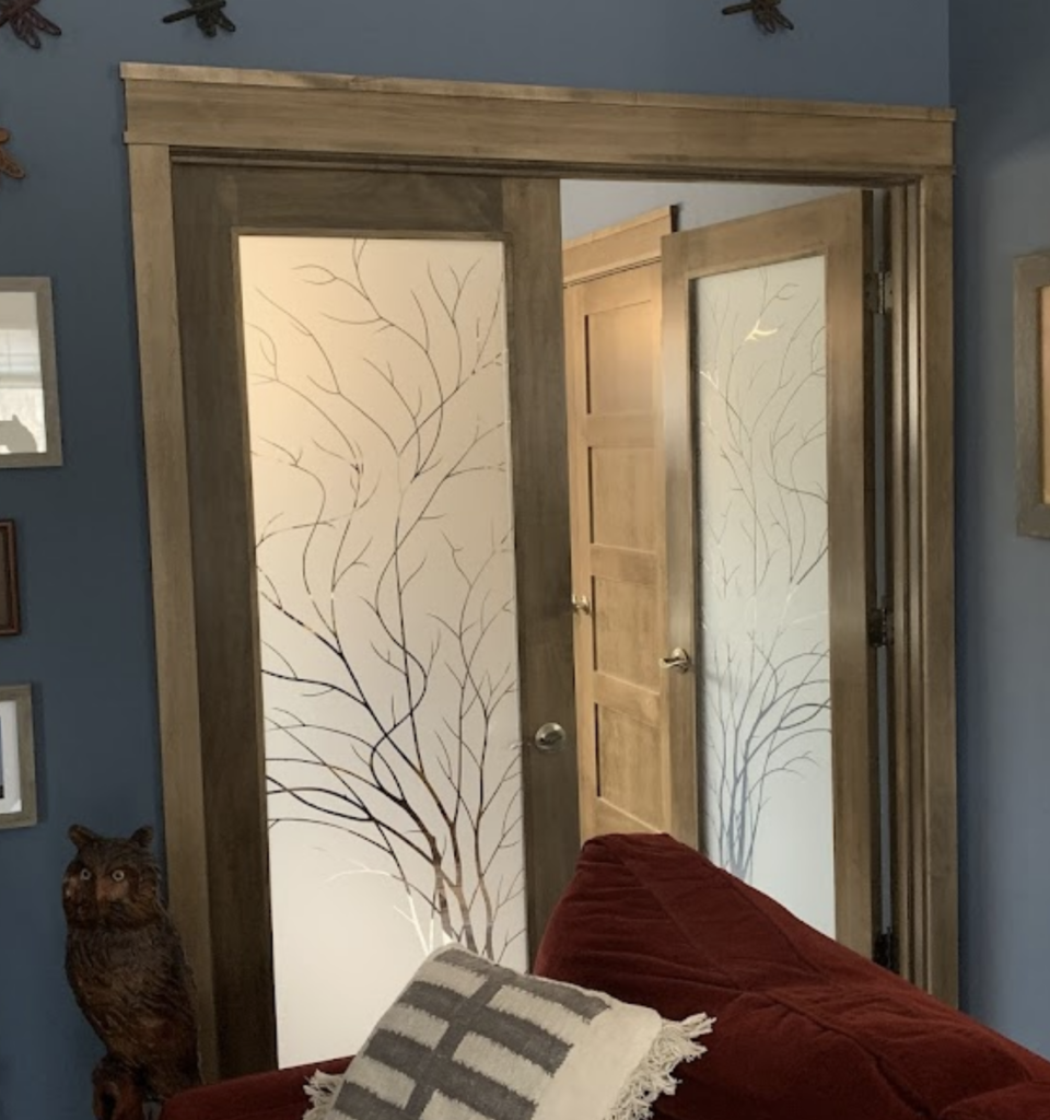 Interior sliding glass door and hinged door with frosted glass etched wispy tree branch 1D negative design, shown in mixed lighting with one door backlit and the other reflecting ambient room light