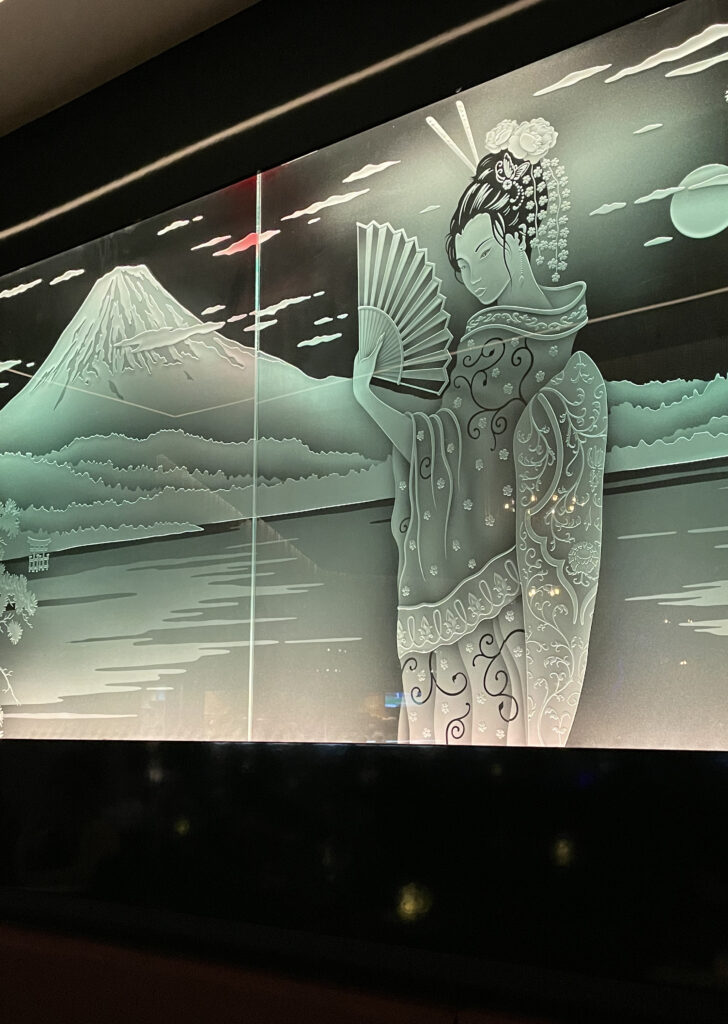 large edge-lit carved glass wall panel featuring geisha and mountain scene illuminated with soft white backlighting