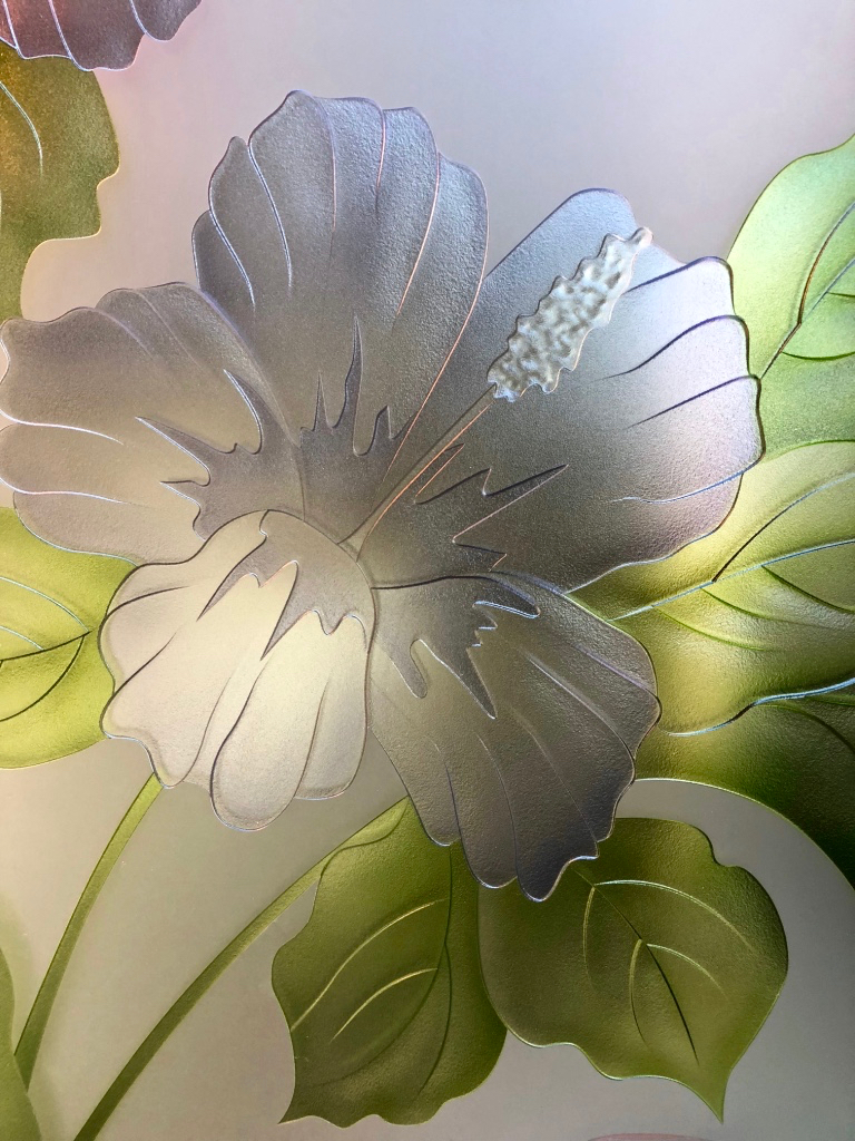 Close-up of elegant hibiscus flower on frosted glass with soft sandblasted texture and delicate carved petal details.