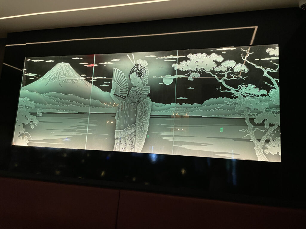 Backlit decorative glass sign with etched geisha design, mountain landscape, and softly illuminated frosted glass panels