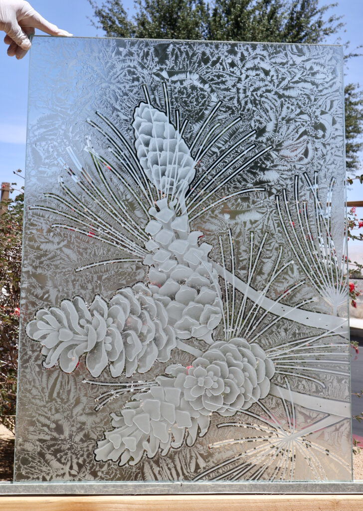 Decorative glass partition panel with detailed 3D carved pine cones, pine needles, and textured frosted glass, creating a custom nature-inspired room divider.