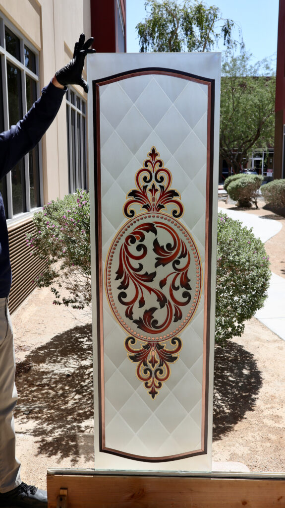 Acid-etched glass panel featuring a full frosted background with sandblasted carved filigree artwork and hand-painted accents, combining privacy with dimensional decorative detail