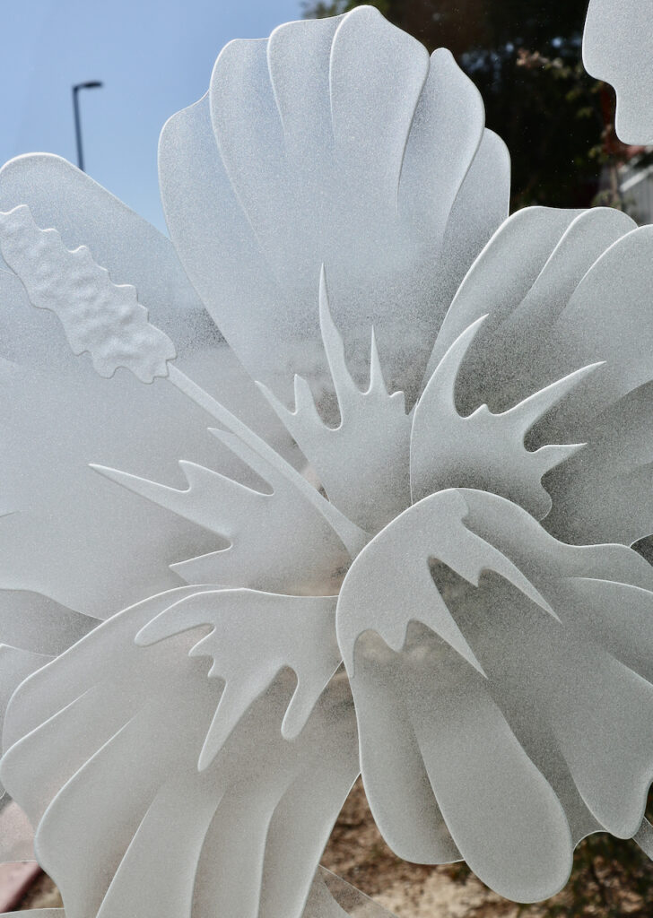 Close-up of sculpted hibiscus petals on 3D carved frosted glass with smooth layered sandblasted texture.