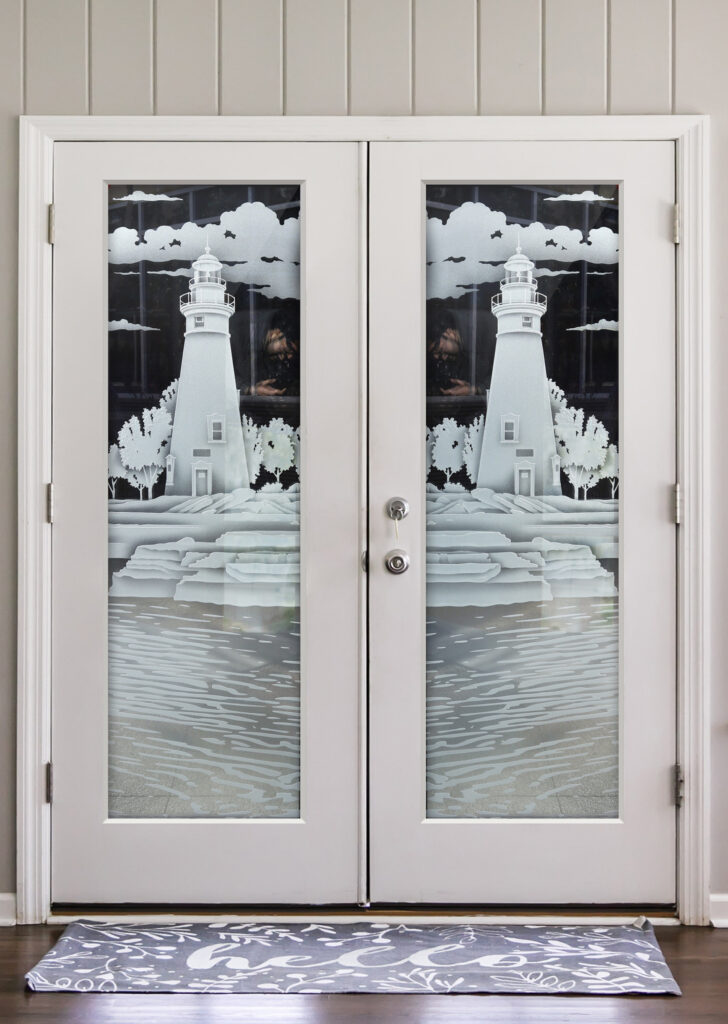 Frosted glass interior pair doors with etched lighthouse, coastal landscape, and ocean water design, creating a dramatic seaside scene with privacy