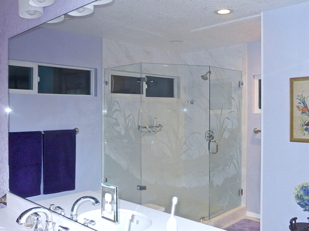 Frameless glass shower enclosure with etched frosted glass design of flowing grasses and reeds creating privacy in a modern bathroom
