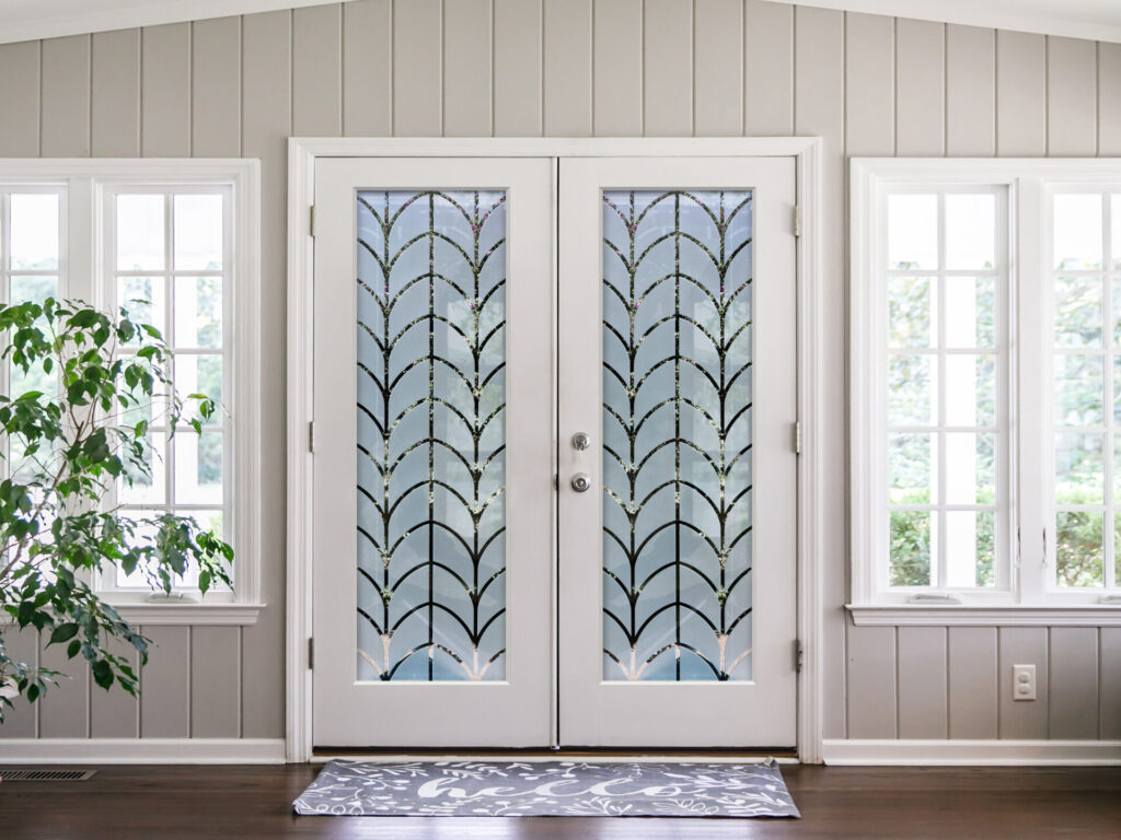 Modern white front double doors with decorative frosted glass featuring a repeating geometric pattern in a light-filled entryway