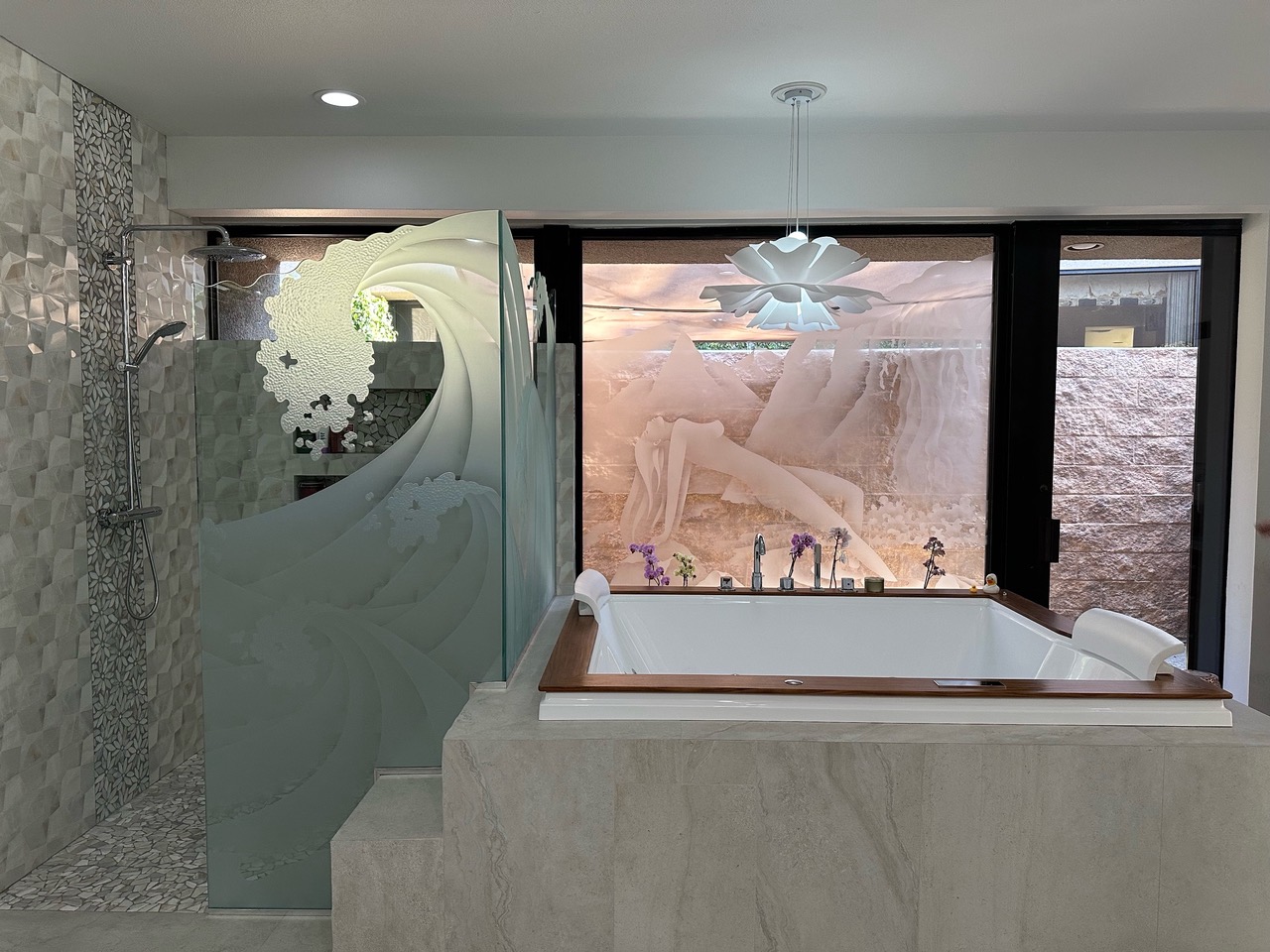 Modern bathroom featuring a frosted glass shower panel with a carved ocean wave design and a large etched glass window depicting an abstract reclining figure behind a built-in soaking tub.