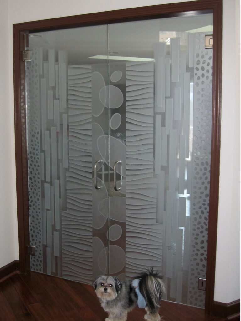 Frameless frosted glass interior double doors with modern etched patterns, with a small dog standing in front of the doors
